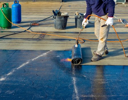 Worker preparing part of bitumen roofing felt roll for melting by gas heater torch flame Worker preparing part of bitumen roofing felt roll for melting by gas heater torch flame